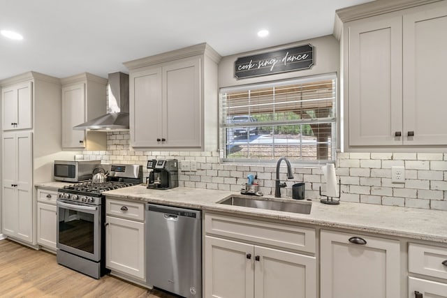 kitchen with wall chimney range hood, stainless steel appliances, decorative backsplash, sink, and light wood-type flooring