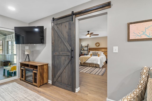 bedroom with ceiling fan, a barn door, and light wood-type flooring