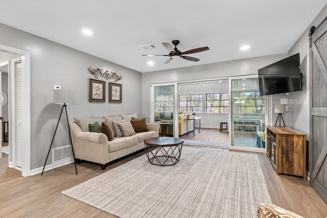 living room featuring ceiling fan, wood-type flooring, and a barn door