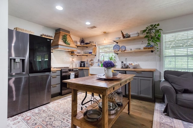 kitchen with appliances with stainless steel finishes, premium range hood, a sink, and open shelves