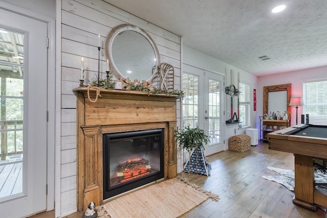 interior space with a glass covered fireplace, wood finished floors, pool table, a textured ceiling, and french doors