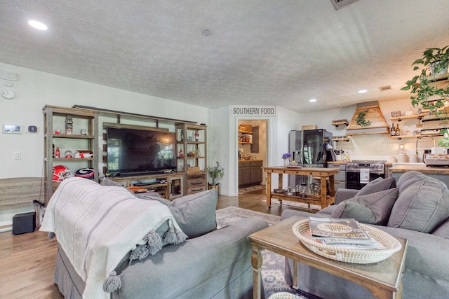 living room featuring recessed lighting, visible vents, a textured ceiling, and wood finished floors