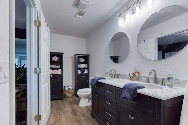 full bath with double vanity, visible vents, toilet, a sink, and wood finished floors