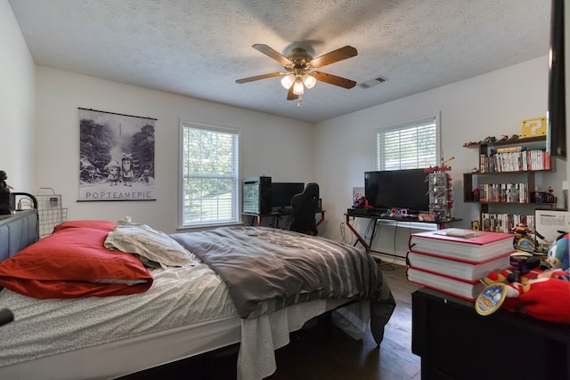 bedroom featuring a ceiling fan, visible vents, a textured ceiling, and wood finished floors