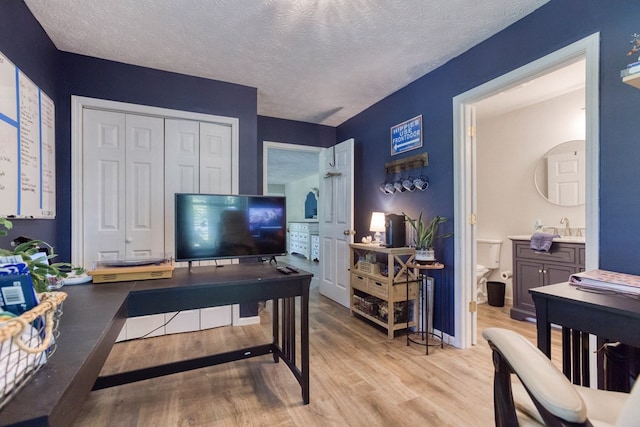 bedroom featuring light wood finished floors, a closet, a sink, a textured ceiling, and ensuite bath