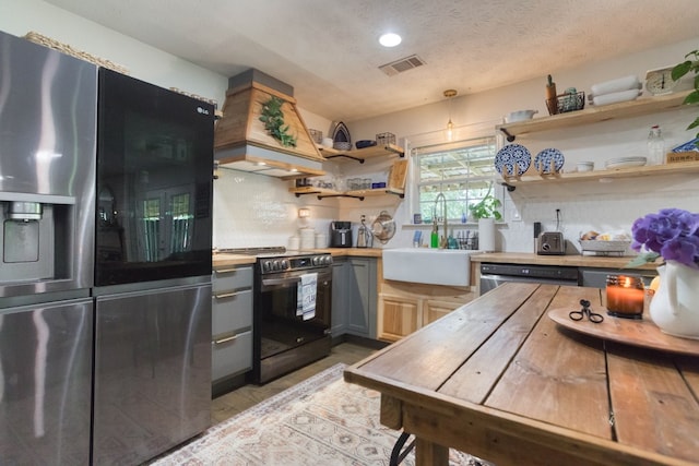 kitchen featuring open shelves, visible vents, appliances with stainless steel finishes, a sink, and premium range hood