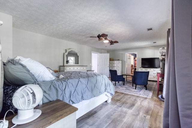 bedroom featuring visible vents, ceiling fan, a textured ceiling, and wood finished floors