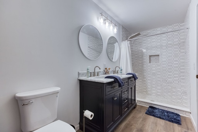 full bathroom featuring vanity, tiled shower, wood finished floors, and toilet