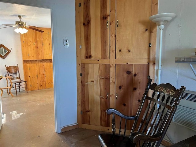 living area featuring concrete floors, ceiling fan, and wood walls