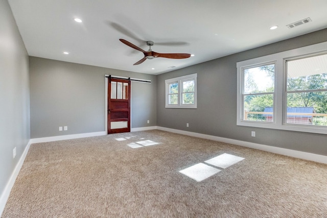 carpeted empty room with ceiling fan and a barn door