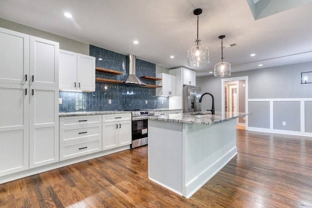 kitchen with wall chimney exhaust hood, an island with sink, decorative light fixtures, white cabinets, and appliances with stainless steel finishes