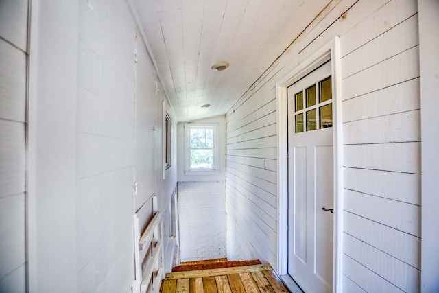 hall with hardwood / wood-style flooring, lofted ceiling, and wood walls