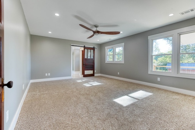 unfurnished bedroom featuring a barn door, carpet floors, and ceiling fan