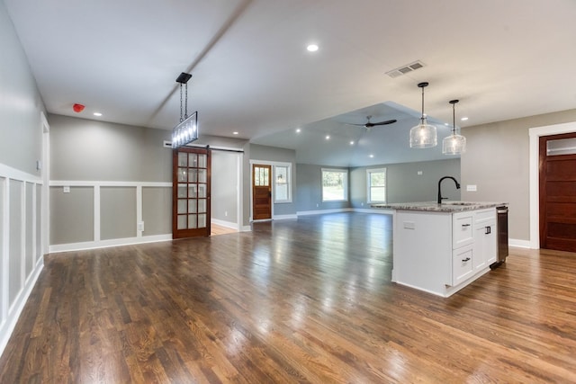 kitchen with light stone counters, pendant lighting, a barn door, a center island with sink, and white cabinetry