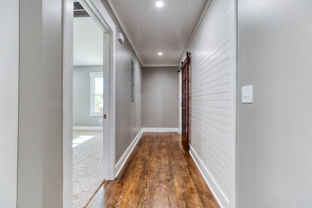 hallway with a barn door, crown molding, and dark wood-type flooring