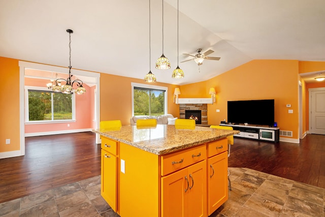 kitchen with a kitchen island, vaulted ceiling, ceiling fan with notable chandelier, dark hardwood / wood-style flooring, and a stone fireplace