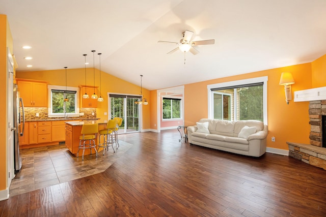 living room featuring vaulted ceiling, dark hardwood / wood-style flooring, ceiling fan, and a stone fireplace