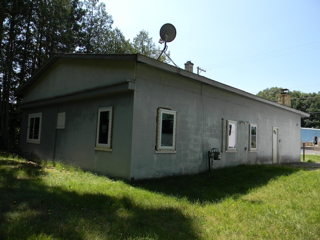 view of home's exterior with concrete block siding, a yard, and a chimney