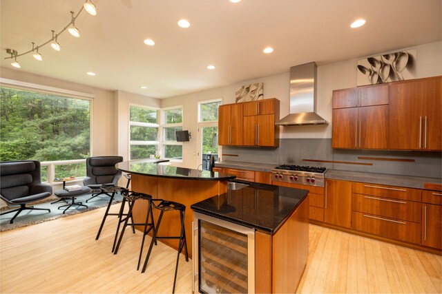 12737 Sanctuary Pl, Grand Haven, MI 49417 - kitchen featuring wine cooler, wall chimney range hood, a center island, stainless steel gas stovetop, and brown cabinetry