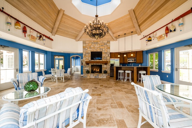 tiled living room with beamed ceiling, wood ceiling, a stone fireplace, an inviting chandelier, and high vaulted ceiling