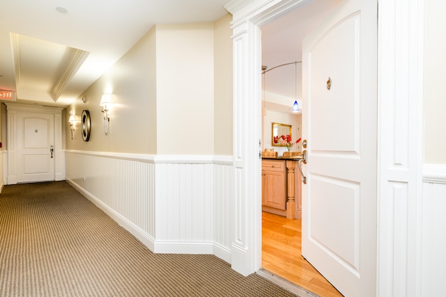 hallway featuring light hardwood / wood-style floors, crown molding, and a tray ceiling