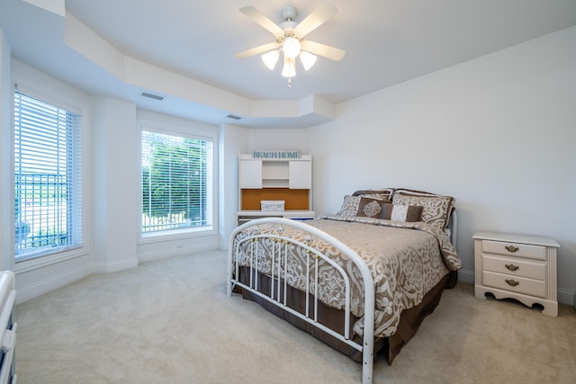 carpeted bedroom with a raised ceiling and ceiling fan