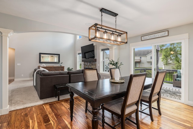 dining room featuring ornate columns, a stone fireplace, and light wood-type flooring