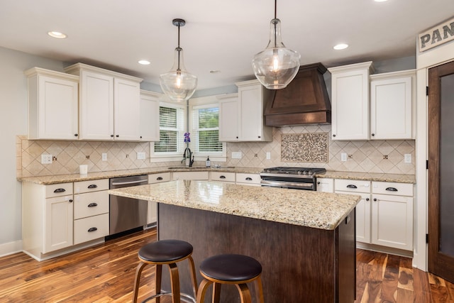 kitchen featuring appliances with stainless steel finishes, a center island, custom range hood, dark hardwood / wood-style flooring, and decorative light fixtures