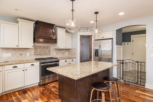 kitchen featuring dark wood-type flooring, decorative light fixtures, a center island, custom range hood, and stainless steel appliances