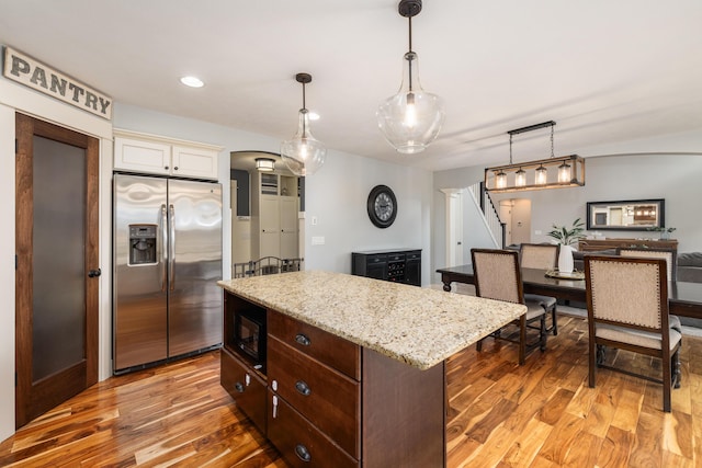 kitchen featuring stainless steel refrigerator with ice dispenser, dark brown cabinetry, hanging light fixtures, a kitchen island, and hardwood / wood-style flooring