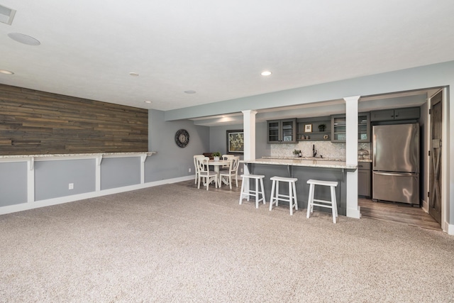 kitchen with a breakfast bar area, stainless steel refrigerator, dark colored carpet, tasteful backsplash, and kitchen peninsula