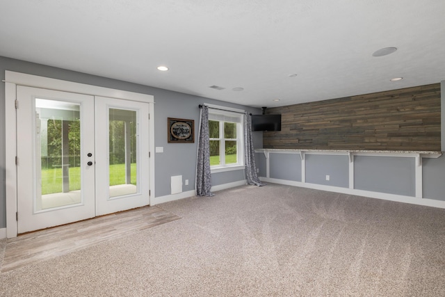 unfurnished living room featuring wooden walls, french doors, and carpet flooring