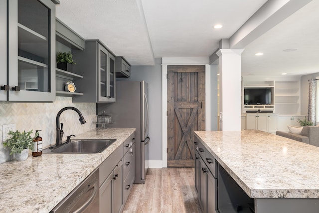 kitchen with sink, light wood-type flooring, dishwasher, light stone countertops, and decorative backsplash