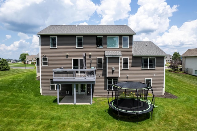 back of property featuring a patio area, a wooden deck, a trampoline, and a lawn