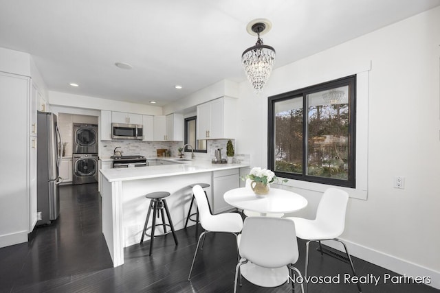 dining area featuring an inviting chandelier, stacked washer / drying machine, dark hardwood / wood-style floors, and sink