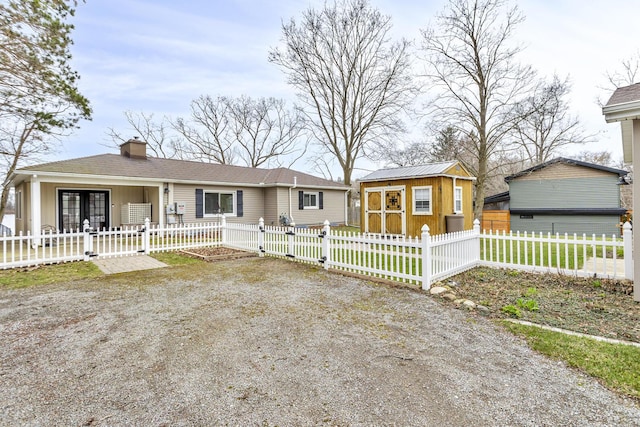 single story home with a gate, a chimney, an outbuilding, and a fenced front yard