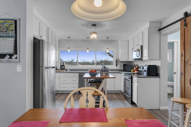 kitchen with stainless steel appliances, a barn door, white cabinetry, and dark countertops
