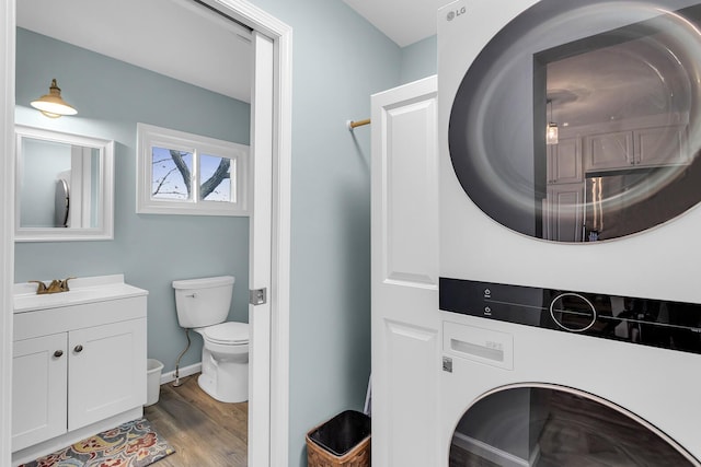 bathroom featuring baseboards, toilet, stacked washer and clothes dryer, vanity, and wood finished floors