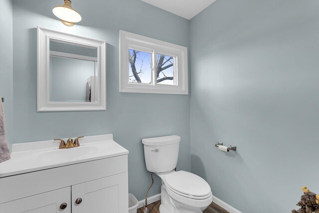 half bathroom with vanity, baseboards, toilet, and wood finished floors