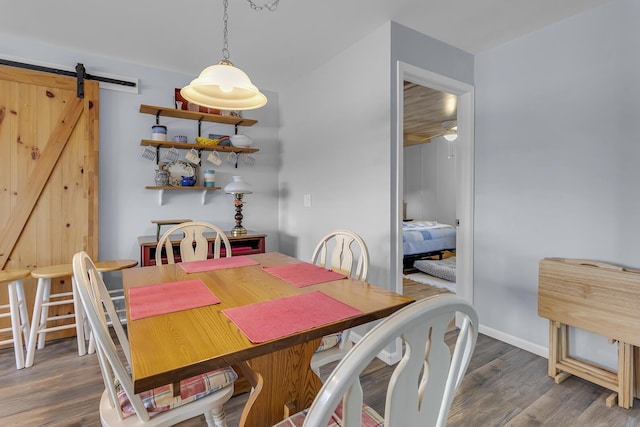 dining room featuring a barn door, baseboards, a ceiling fan, and wood finished floors