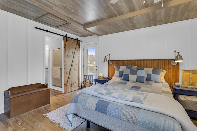 bedroom featuring a decorative wall, ensuite bathroom, a barn door, wood finished floors, and wooden ceiling