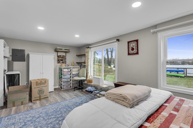 bedroom with electric panel, recessed lighting, a water view, and wood finished floors