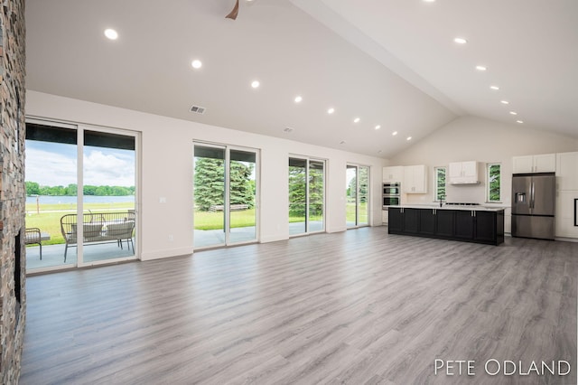 unfurnished living room featuring high vaulted ceiling and light hardwood / wood-style floors