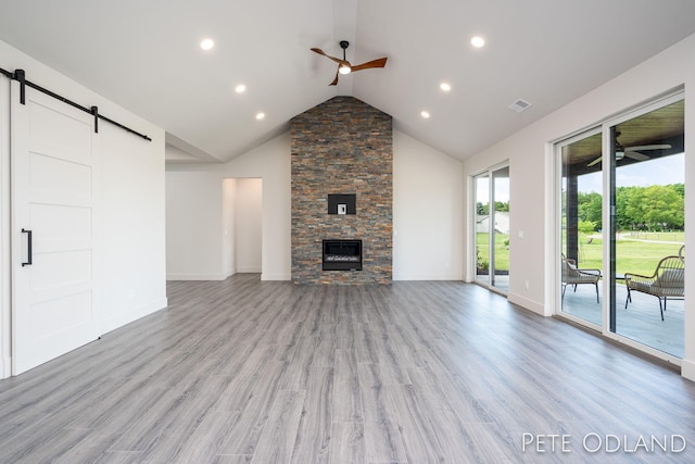 unfurnished living room featuring vaulted ceiling, a fireplace, ceiling fan, light hardwood / wood-style floors, and a barn door