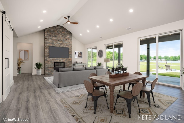 dining space with a barn door, high vaulted ceiling, a fireplace, and light hardwood / wood-style flooring