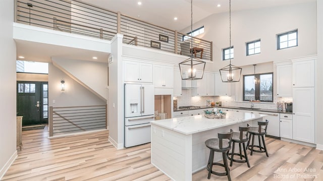 kitchen featuring white appliances, white cabinetry, backsplash, high vaulted ceiling, and a center island