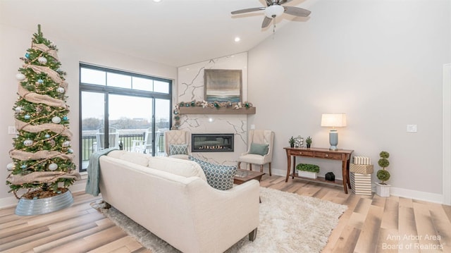 living room with ceiling fan, lofted ceiling, a high end fireplace, and light hardwood / wood-style flooring