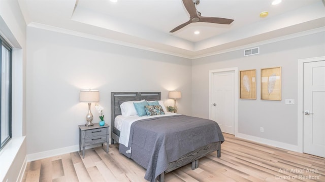 bedroom featuring crown molding, a tray ceiling, light hardwood / wood-style floors, and ceiling fan