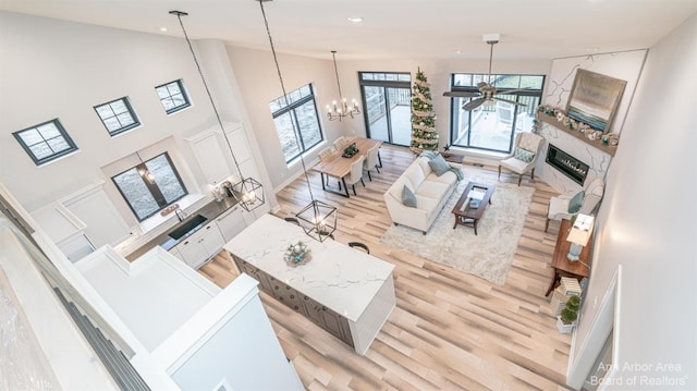 living room featuring a high ceiling, ceiling fan with notable chandelier, and light hardwood / wood-style floors