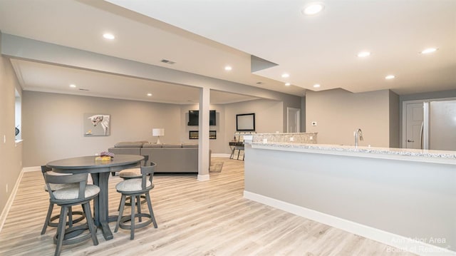 kitchen with sink, a breakfast bar area, light stone counters, white fridge, and light hardwood / wood-style floors